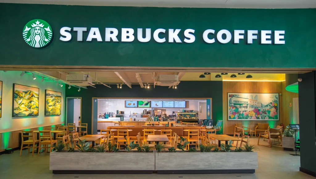 Frente de uma loja da starbucks com as cores verde e branco. Lugar parece aconchegante.